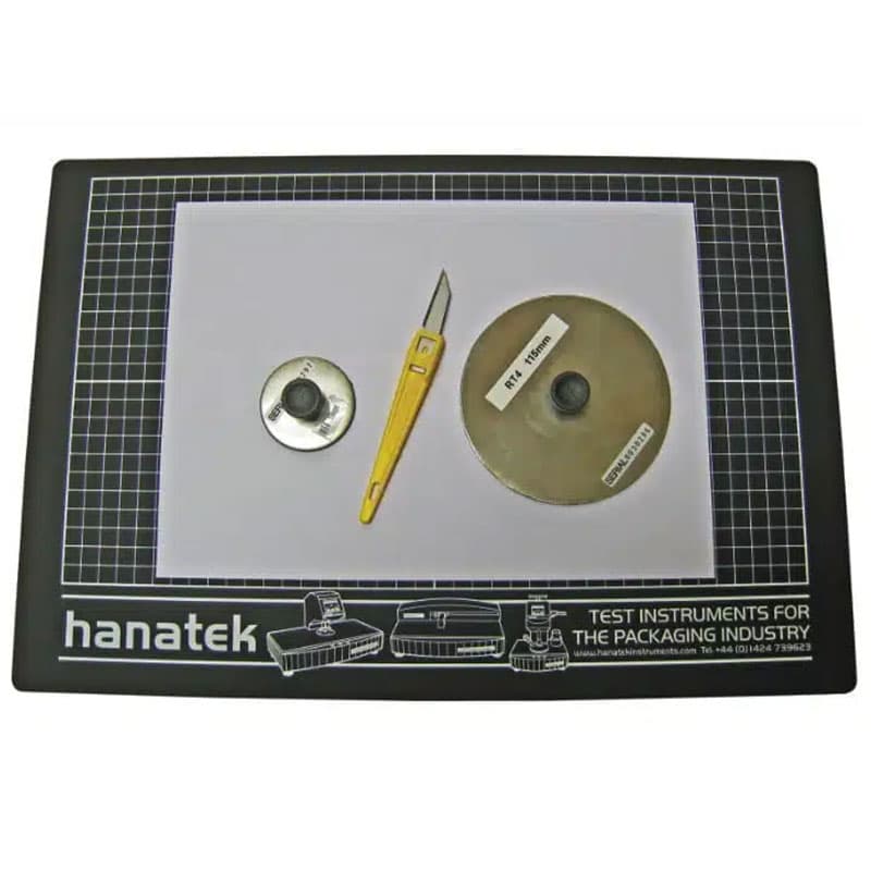 Cutting mat with sample preparation tools – A Hanatek-branded cutting mat with a yellow cutting knife and circular sample cutting discs, used for preparing material samples for abrasion testing.