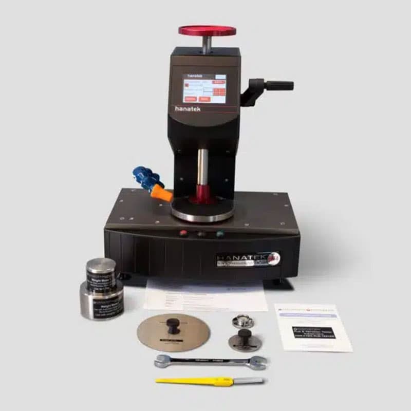 Hanatek RT4 Rub & Abrasion Tester with accessories – A black abrasion testing machine with a digital touchscreen display, accompanied by cutting tools, test weights, a wrench, and printed instructions.
