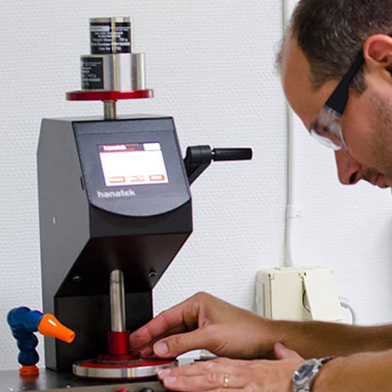 Technician operating the Hanatek RT4 tester – A laboratory technician wearing safety glasses carefully adjusting a test sample on the digital abrasion testing machine.