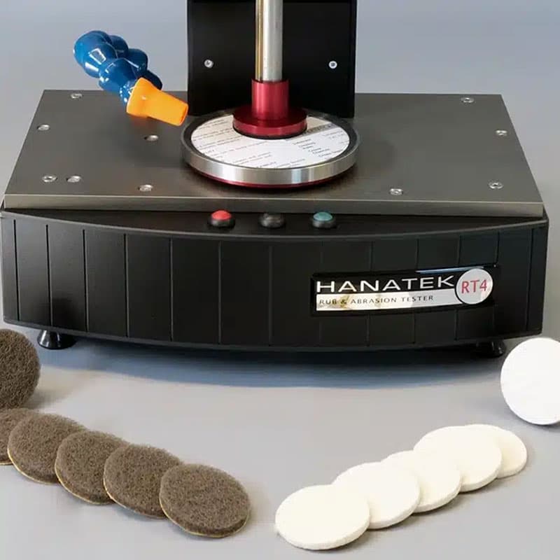 Hanatek RT4 Rub & Abrasion Tester with test pads – The machine is displayed with various abrasion pads, including white and brown circular pads, used for different material testing conditions.