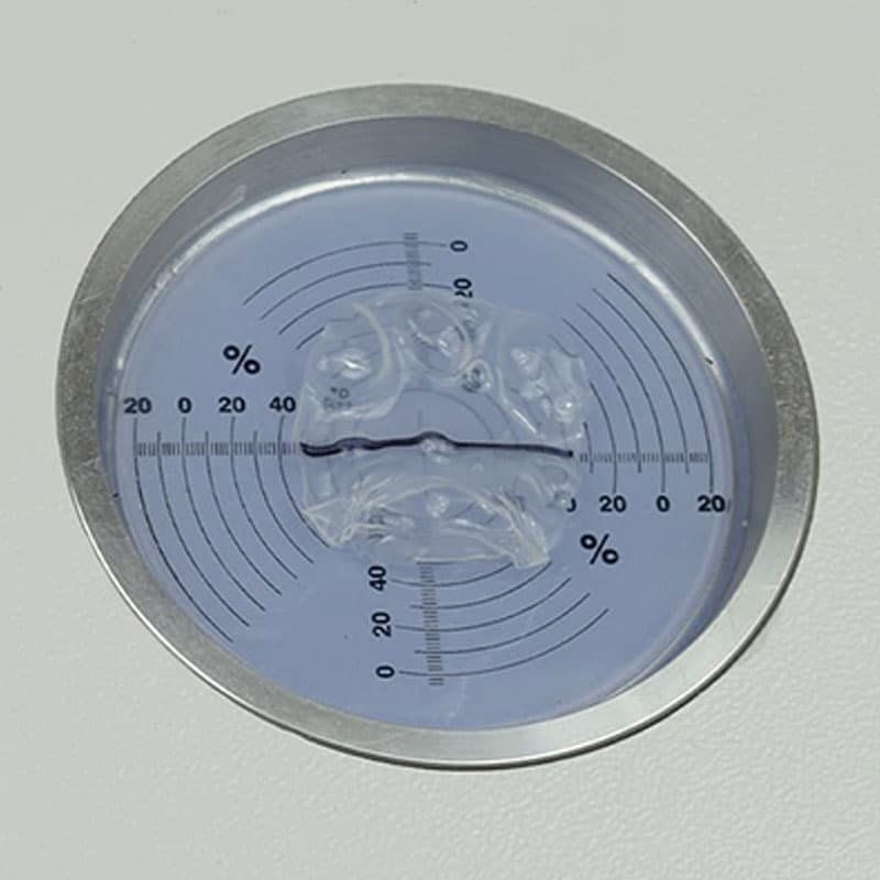 Plastic film shrinkage test sample with measurement grid – A circular test sample in a metal holder, with a blue-tinted plastic film showing shrinkage patterns and a black measurement line.
