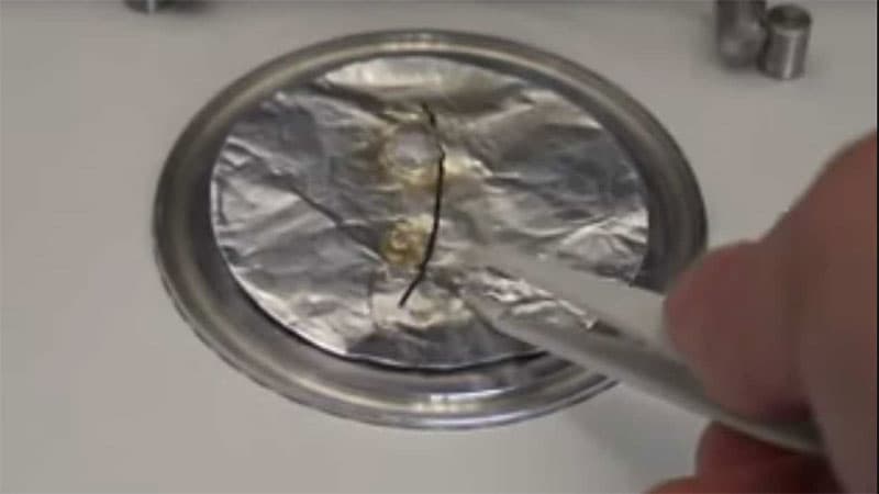 Shrinkage test sample with aluminum foil layer – A metal dish containing a heat-treated aluminum foil sample, showing a black measurement line and deformations from shrinkage.