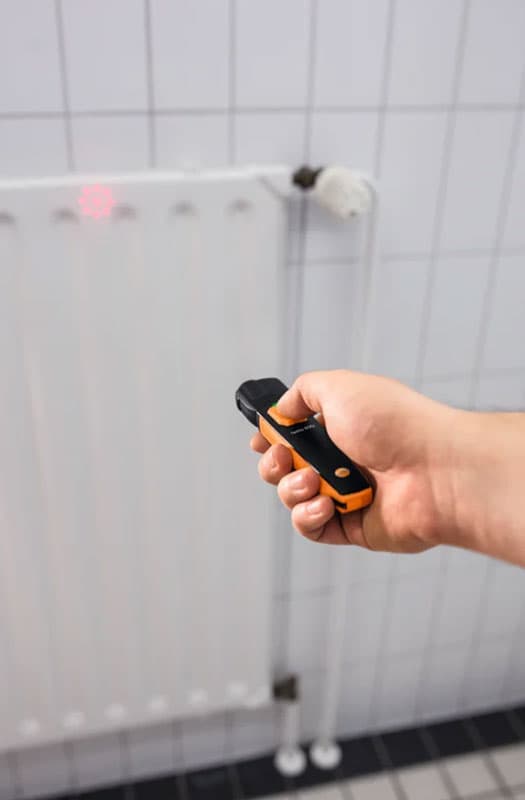 Person using Testo 805i to measure radiator temperature with visible laser marker.