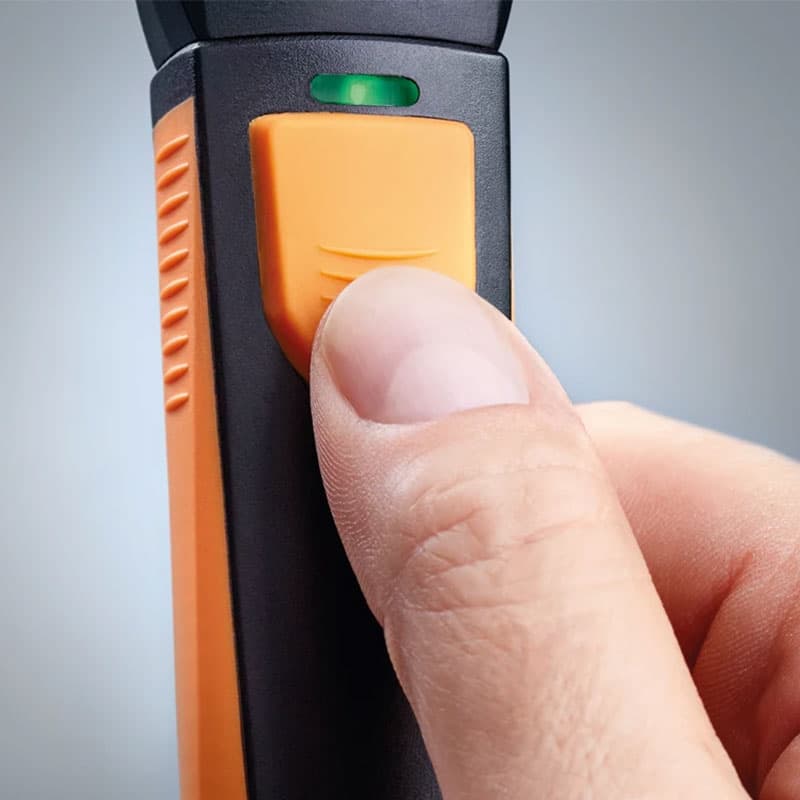 Thumb pressing the trigger button on Testo 805i with green LED indicator light.