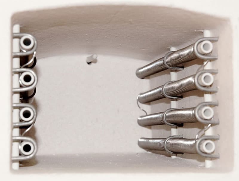 A close-up view of the interior of a muffle furnace, showing metal coil heating elements mounted on the sides of the insulated chamber.