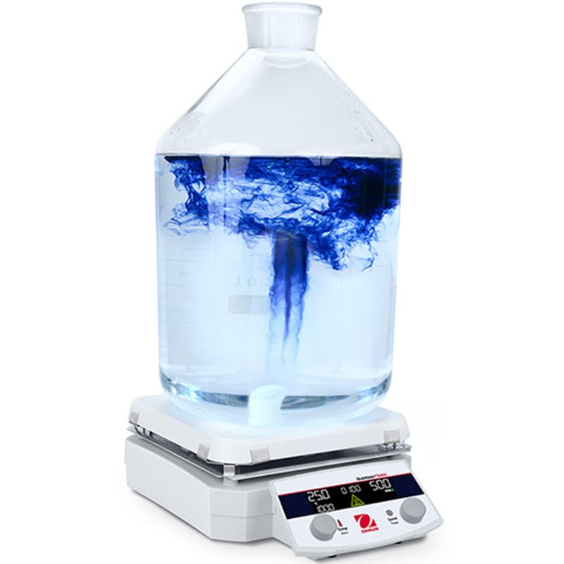 Magnetic stirrer with a large glass container, showing blue dye swirling and mixing into clear water.