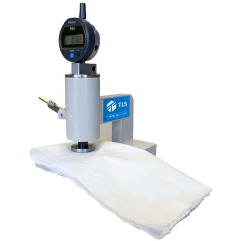 Compression tester measuring the thickness of white material, with a digital Mitutoyo display and TLS logo.