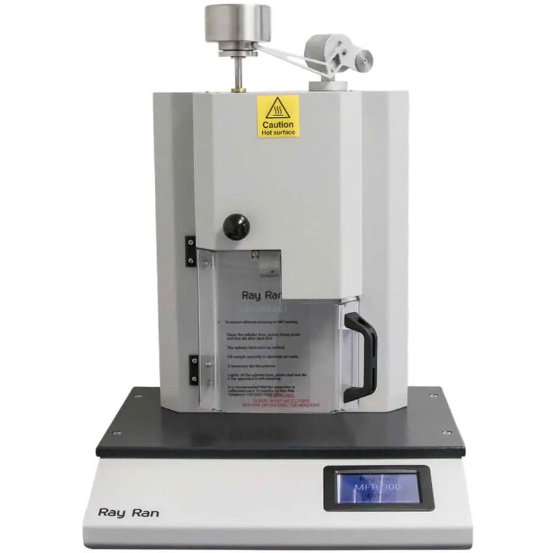 This is a photo of a melt flow indexer. It has a sleek, modern design, primarily composed of white and grey tones with black and silver accents. The machine is labelled "Ray Ran" at the base, with a digital display screen and a caution label indicating a hot surface on the upper part. The background is plain white, making the device the clear focal point.