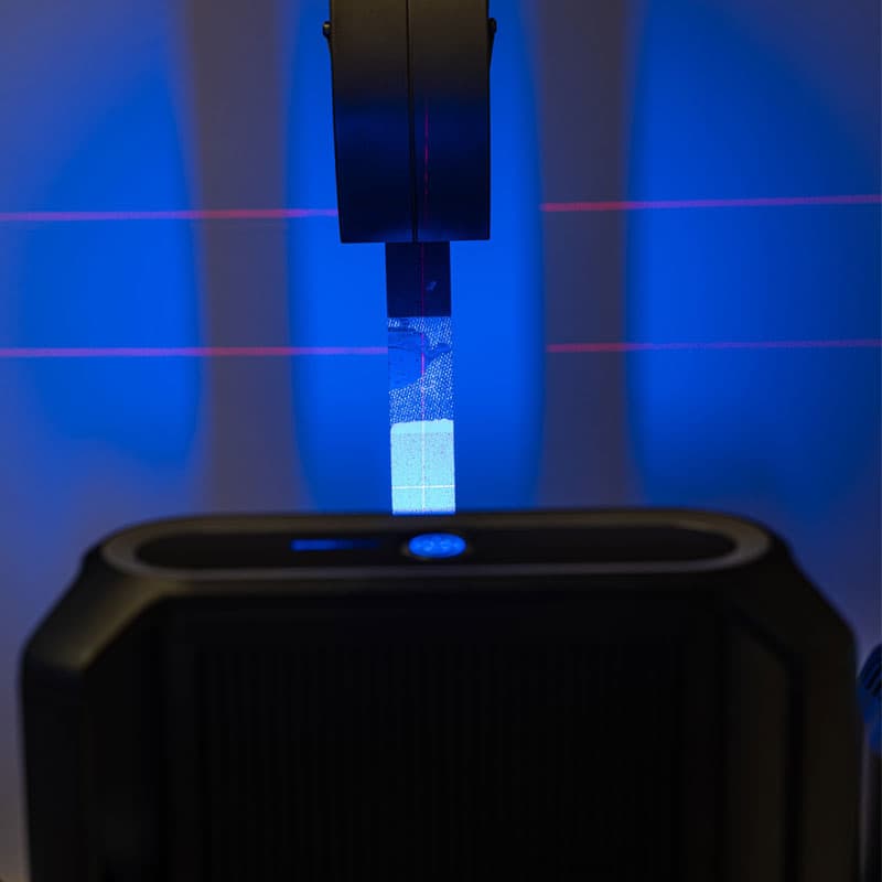 Close-up of a tensile testing setup with blue illumination and red laser alignment beams on the sample.
