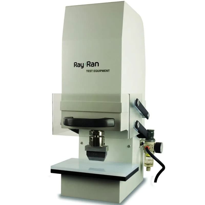 Compact Ray-Ran test equipment machine with a protective housing, transparent safety guard, manual/pneumatic lever, and flat working surface for cutting or material preparation in laboratory settings.