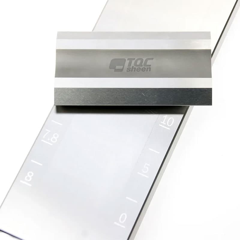 Close-up of the TQC Sheen wet film thickness gauge with logo and precision-etched measurement markings on a stainless steel surface.