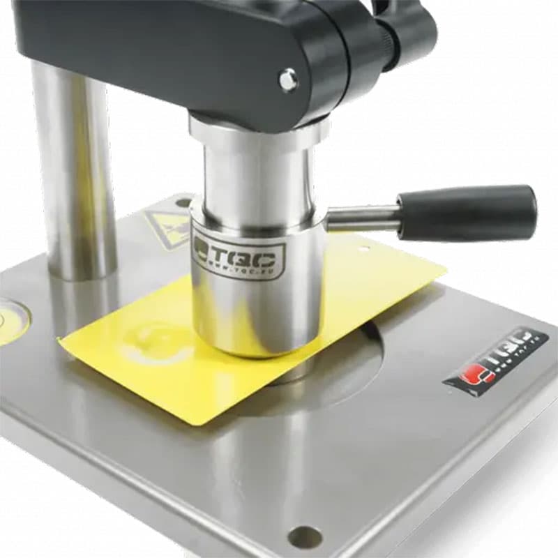 Close-up of TQC Sheen coating thickness gauge pressing onto a yellow-coated sample, with a stainless steel head and ergonomic handle.