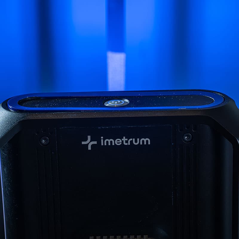 Close-up of a UVX3D device's top panel with imetrum logo and a circular marker, under a blue-lit background.