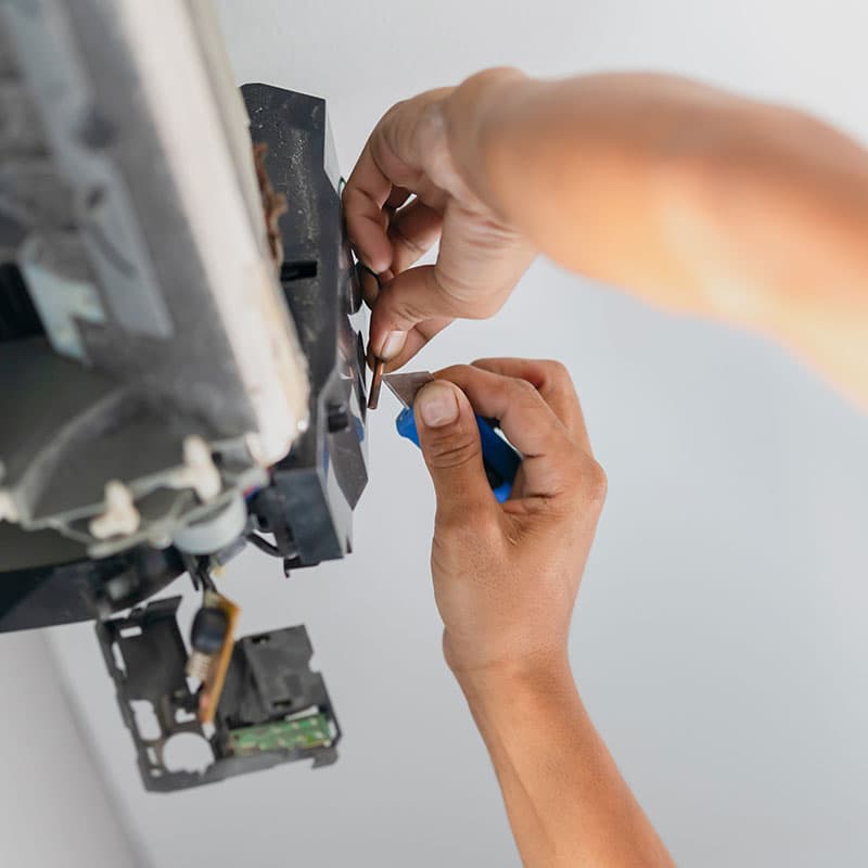Person using a screwdriver to repair an thermistor on a wall, with visible internal components and disassembled parts.