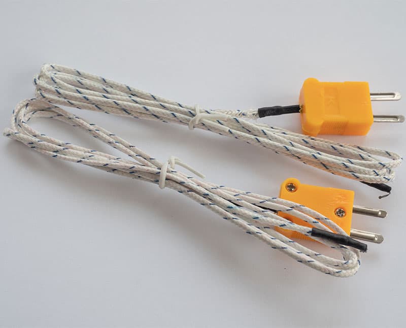 Two thermocouple wires with yellow connectors and white braided cables tied with twist ties, placed on a white surface.