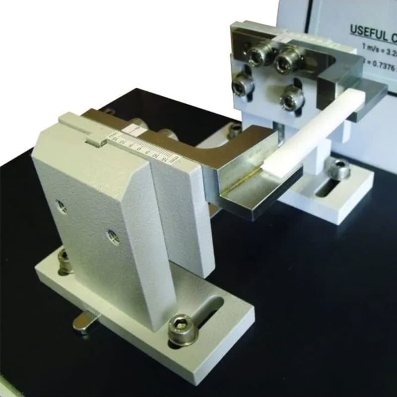 A close-up of the Ray-Ran impact tester's sample-holding fixture, securing a white sample piece for testing.