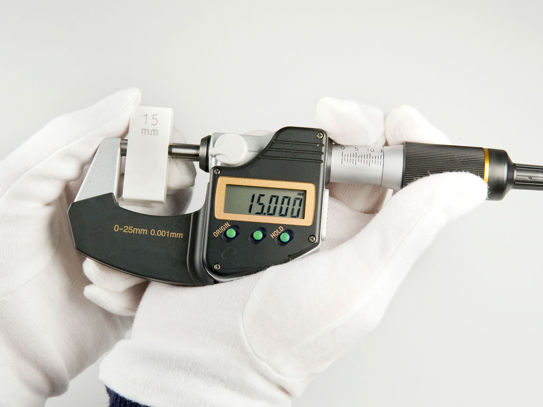 Digital micrometer measuring a 15 mm gauge block, displaying a reading of 15.000 mm.