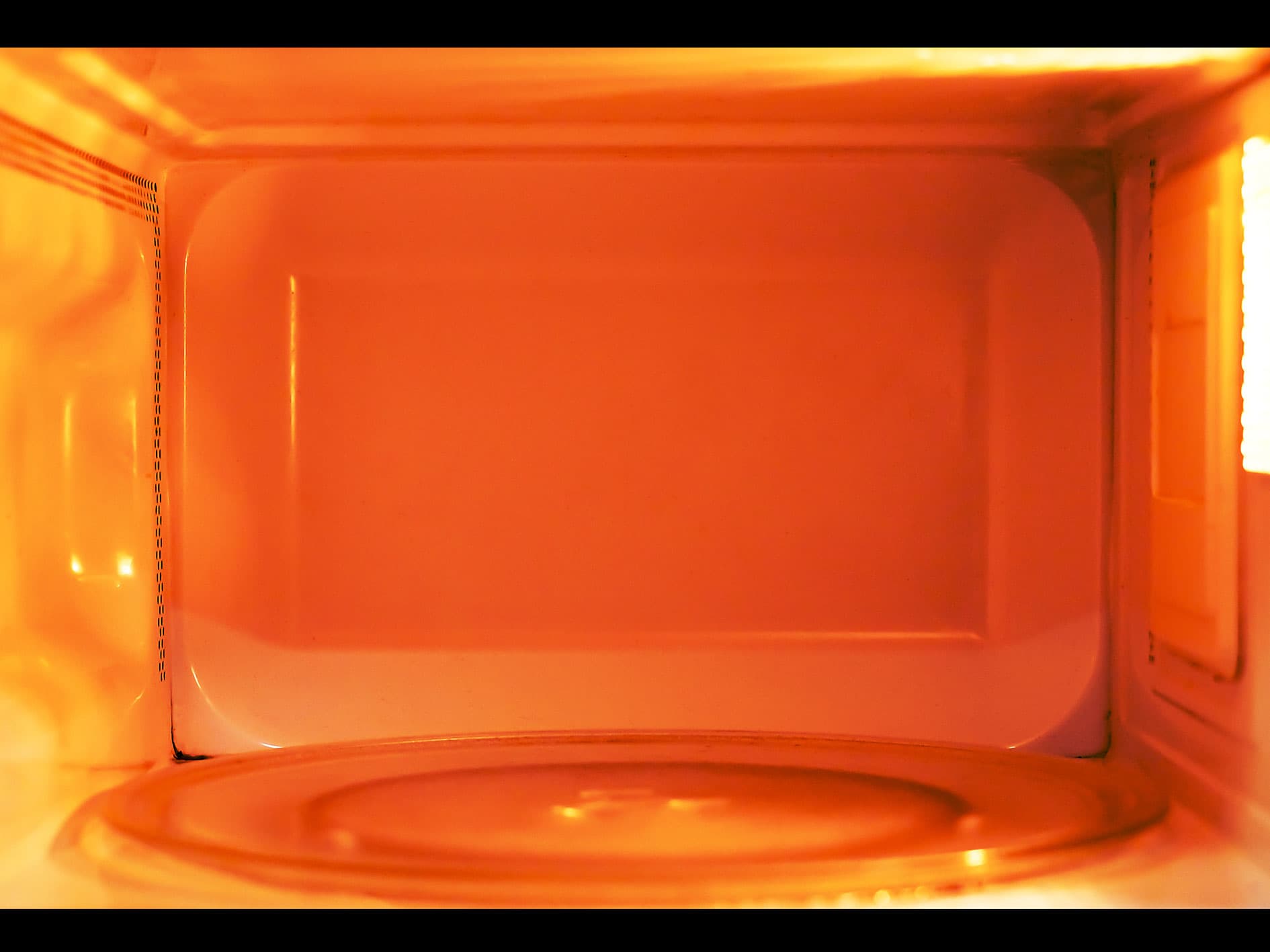 Interior of a microwave oven glowing with orange light during operation with glass turntable inside the cooking chamber.
