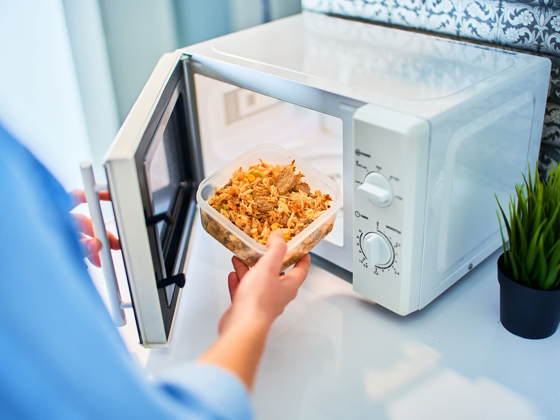 Person placing a container of rice and vegetables into a microwave oven to reheat food.
