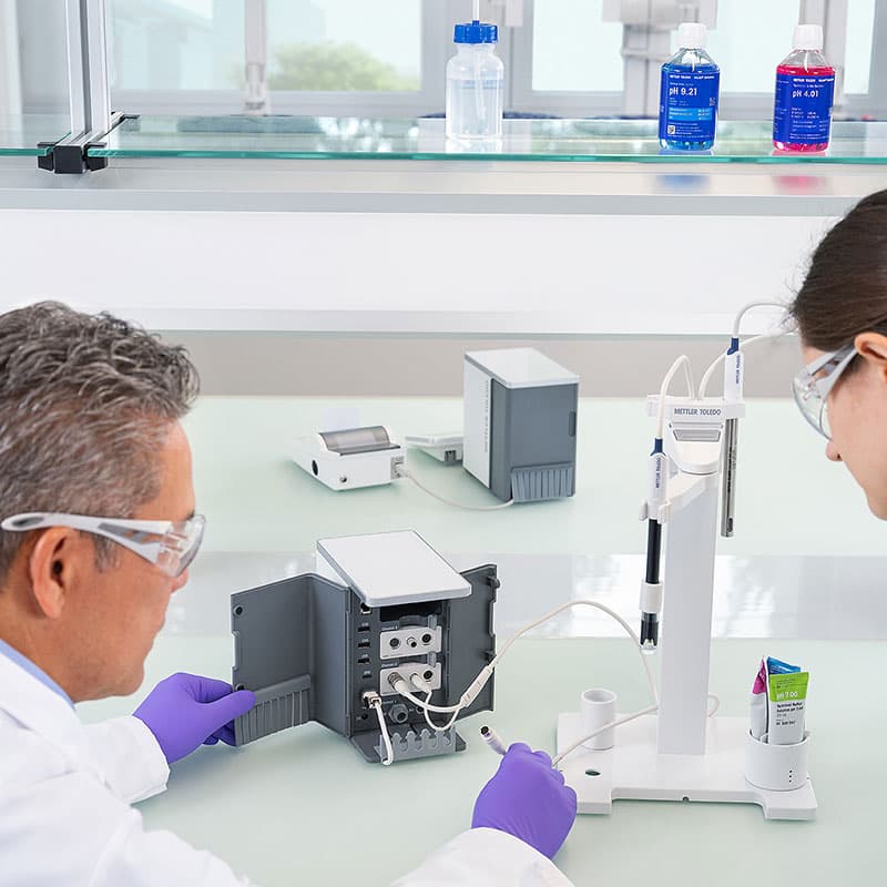 Laboratory technicians setting up METTLER TOLEDO NineFocus system with open rear panel, connecting sensor cables and pH electrode in modern lab environment.