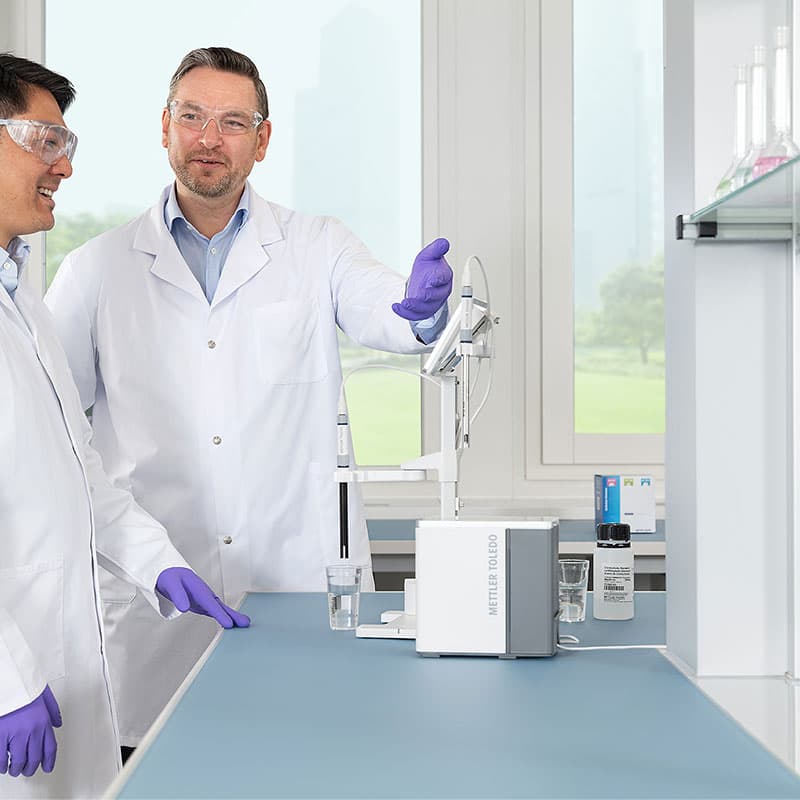 Two laboratory professionals discussing results while using METTLER TOLEDO NineFocus pH meter with probe in beaker on lab bench.