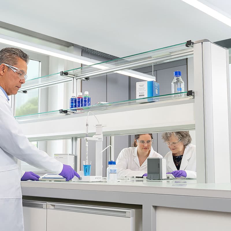 Laboratory team using METTLER TOLEDO NineFocus pH measurement system with electrode in blue liquid sample and touchscreen display in modern lab setting.