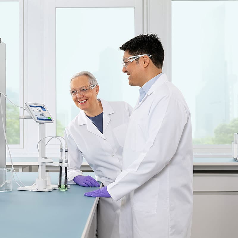 Two laboratory professionals using METTLER TOLEDO NineFocus pH meter to measure green liquid sample while reviewing digital display.