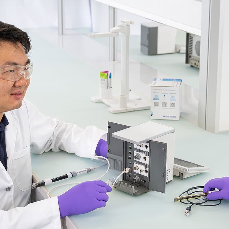 Laboratory technician connecting sensor cable to METTLER TOLEDO NineFocus unit with doors open showing modular ports and interface connections.