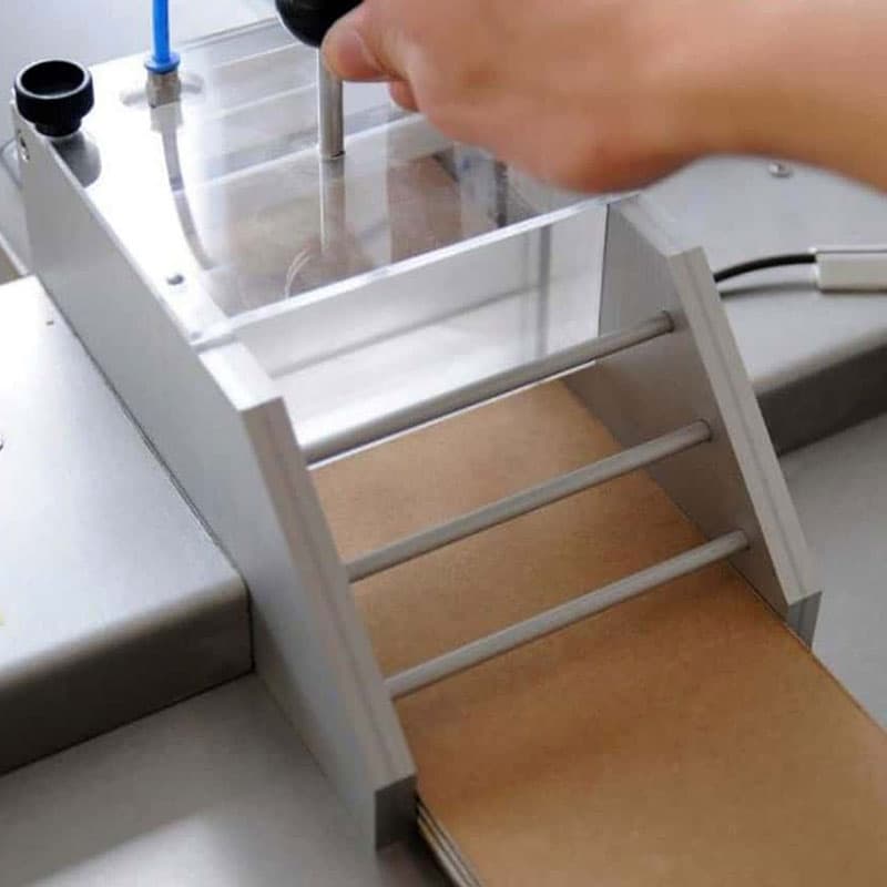 Close-up of ECT saw cutter feeding corrugated board into cutting guide with hand pressing top plate.