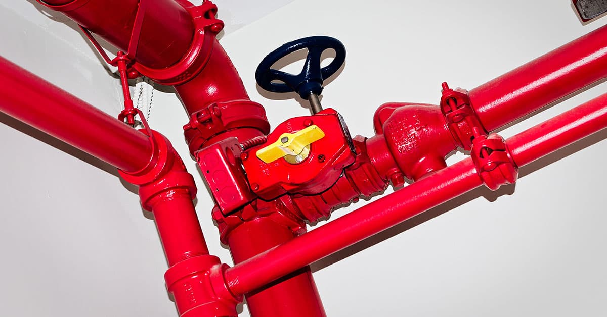 Red fire sprinkler pipes with valves and control wheel mounted overhead.
