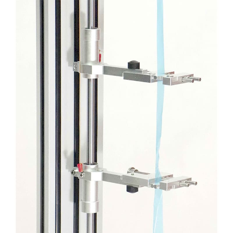 Close-up of a Barrus ElastExt Contact Extensometer showing two adjustable metal measuring arms with contact probes positioned against a vertical light-blue test specimen.