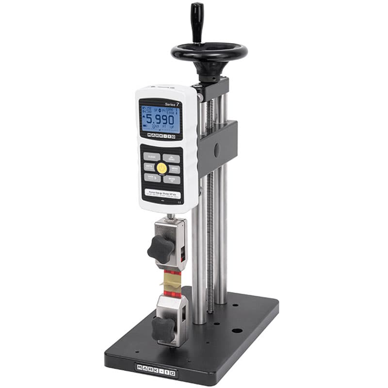 Mark-10 ES20 manual force test stand with digital force gauge, handwheel-operated carriage, and grips configured for tension testing.