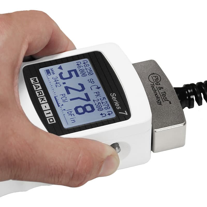 Mark-10 M7i digital force/torque indicator held in hand with a Plug & Test sensor connected and force measurement displayed.