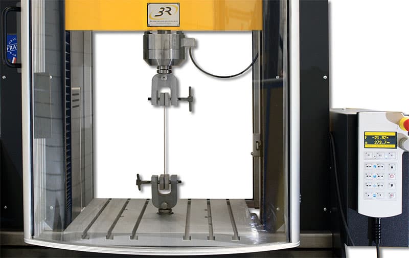 Close-up of the SYNTAX 12 Universal Testing Machine – 12 kN with a specimen secured between upper and lower grips and a digital control panel on the right.