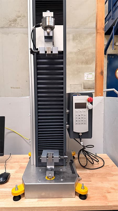 Close front view of the SYNTAX 5 compact 5 kN universal testing machine with grips and control unit.