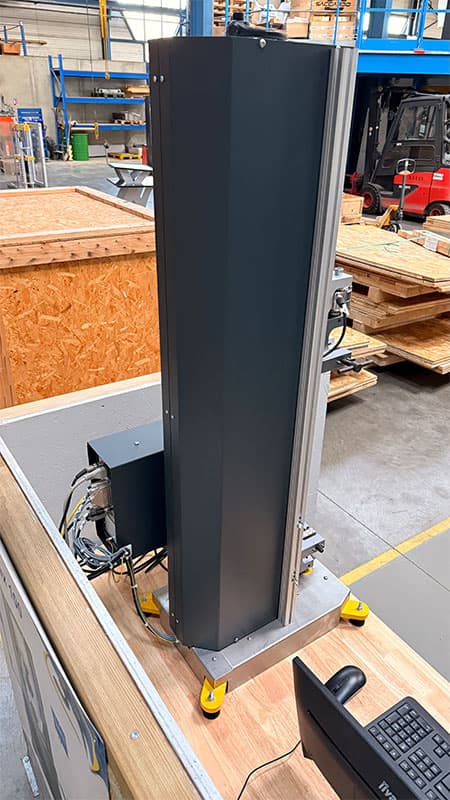 Rear view of the SYNTAX 5 compact 5 kN universal testing machine showing its vertical frame and enclosed housing.