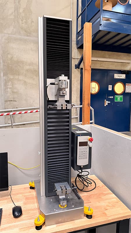 Front-right view of the SYNTAX 5 compact 5 kN universal testing machine with test grips and controller.