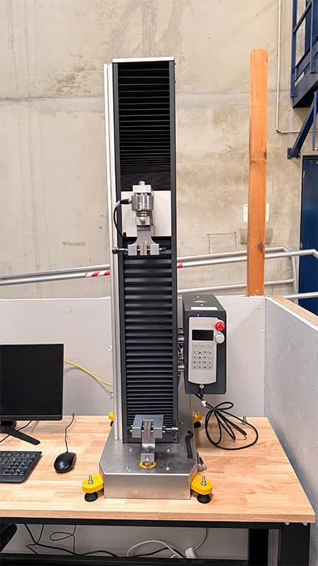Full front view of the SYNTAX 5 compact 5 kN universal testing machine with vertically aligned test grips.