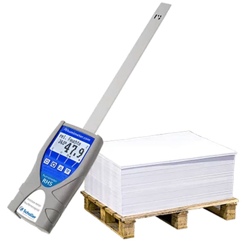 Digital moisture meter 'RH5' by Schaller measuring relative humidity, displayed next to a stack of white paper sheets on a wooden pallet.