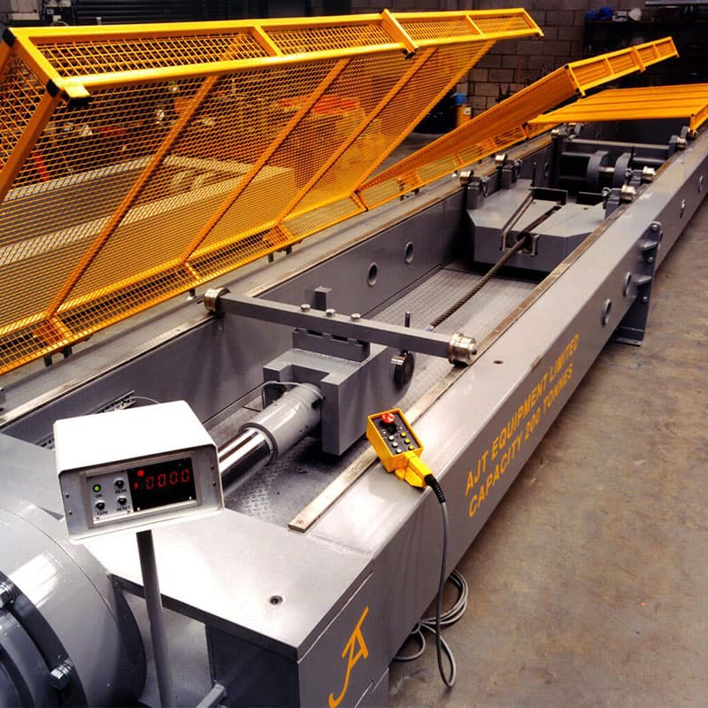 Grey horizontal tensile tester with yellow mesh cover, digital readout, and manual control pendant.