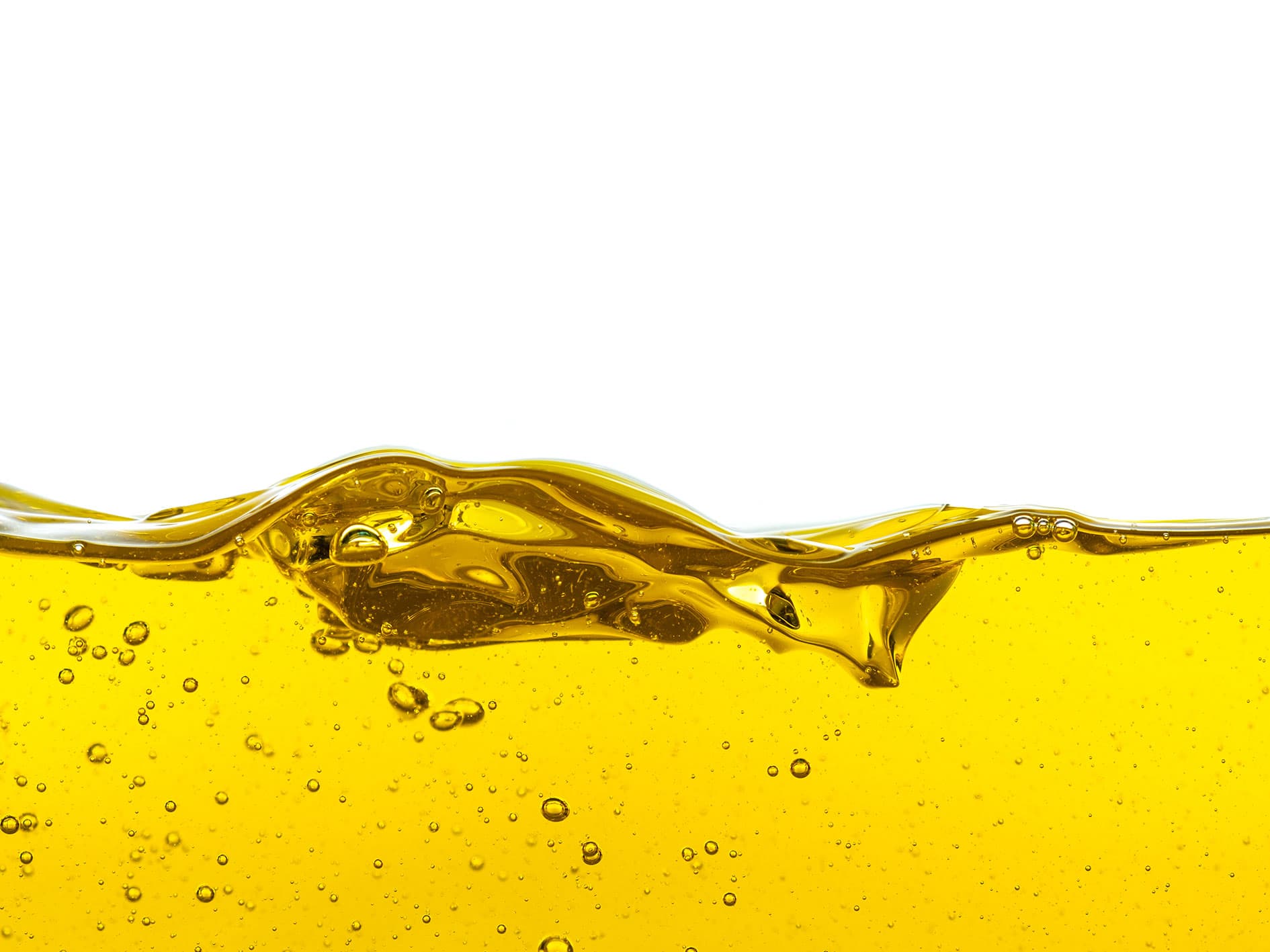 Close-up of golden liquid with bubbles in motion – A transparent yellow-gold fluid, possibly oil or syrup, forming a smooth wavy surface with tiny air bubbles suspended inside, against a clean white background.