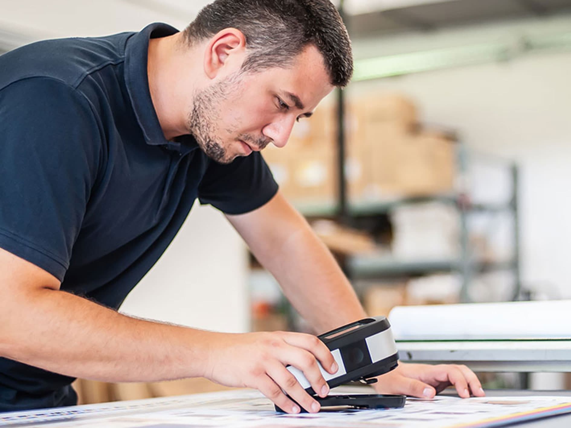 Technician using a handheld spectrophotometer for colour quality control on a print sheet.