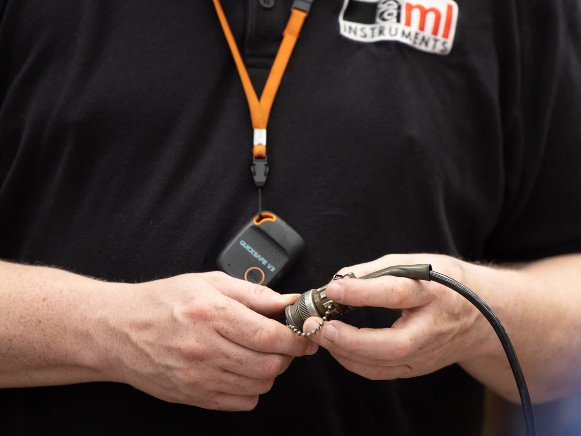 Technician connecting a cable to a sensor while wearing AML Instruments uniform and lanyard.