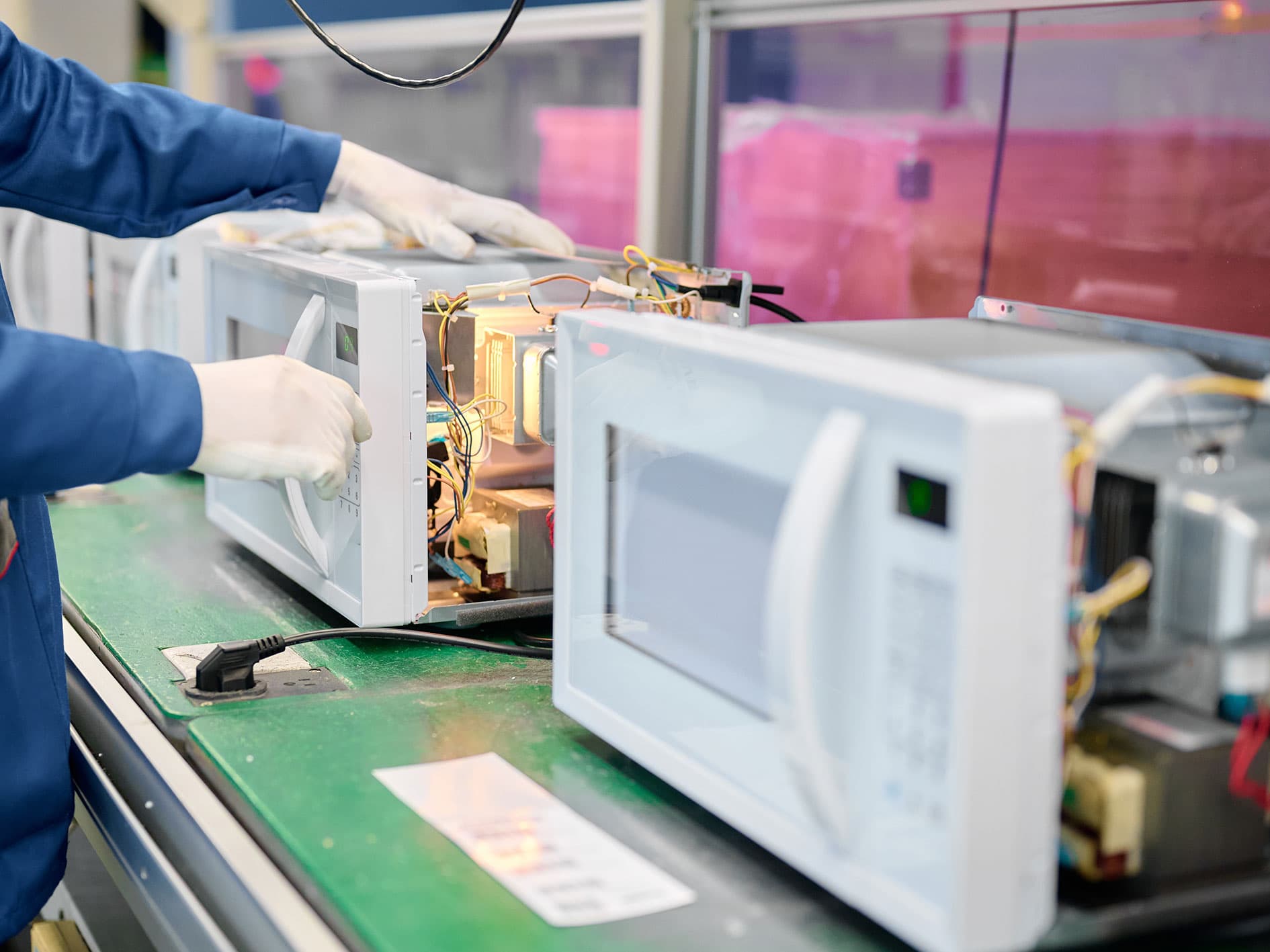Technician repairing microwave ovens with exposed internal components on a workshop assembly line.