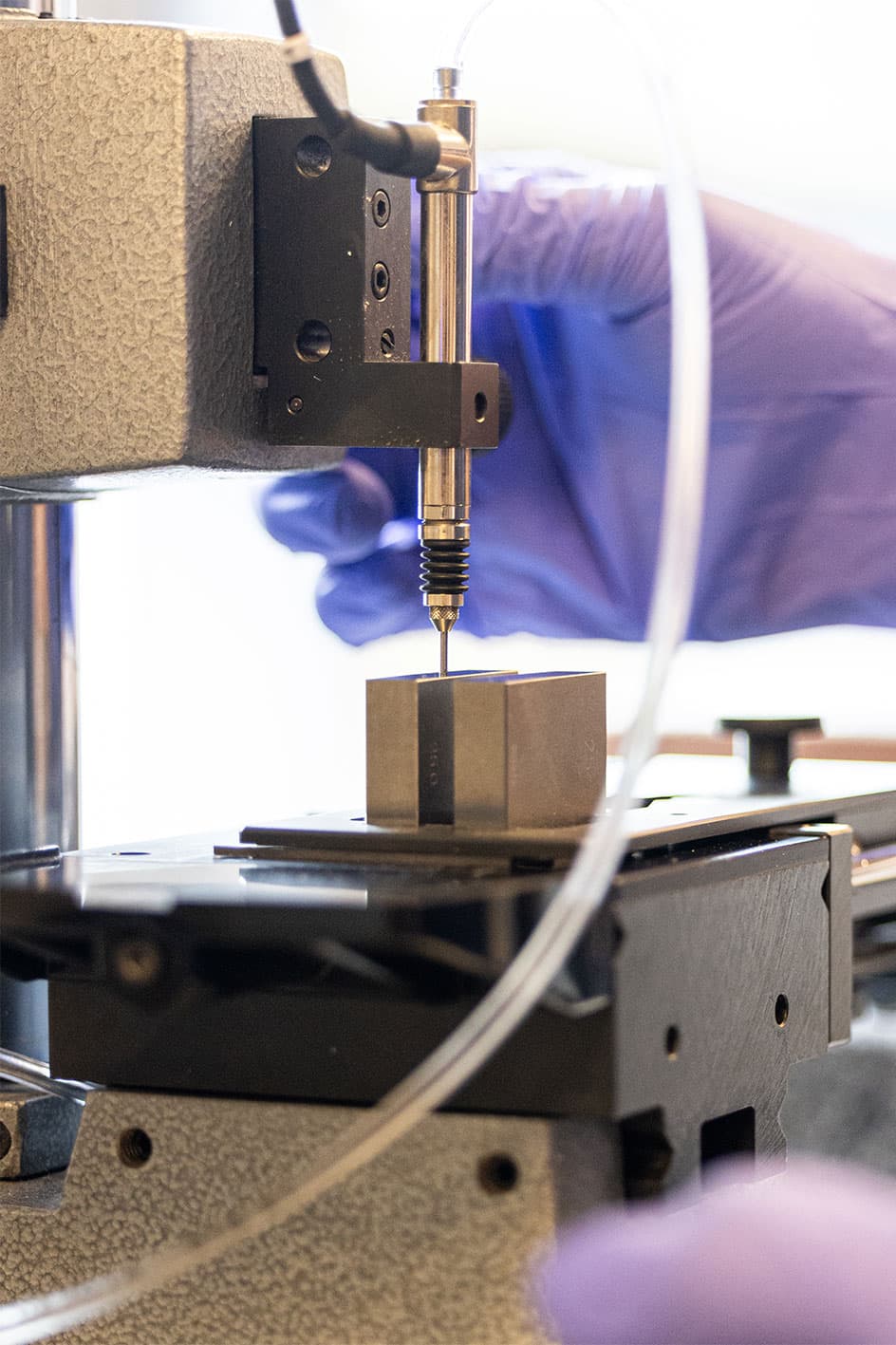 Close-up of hardness testing machine with probe measuring a metal sample block.