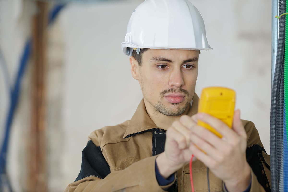 Construction worker in a hard hat using a yellow handheld device to test or measure electrical wiring.