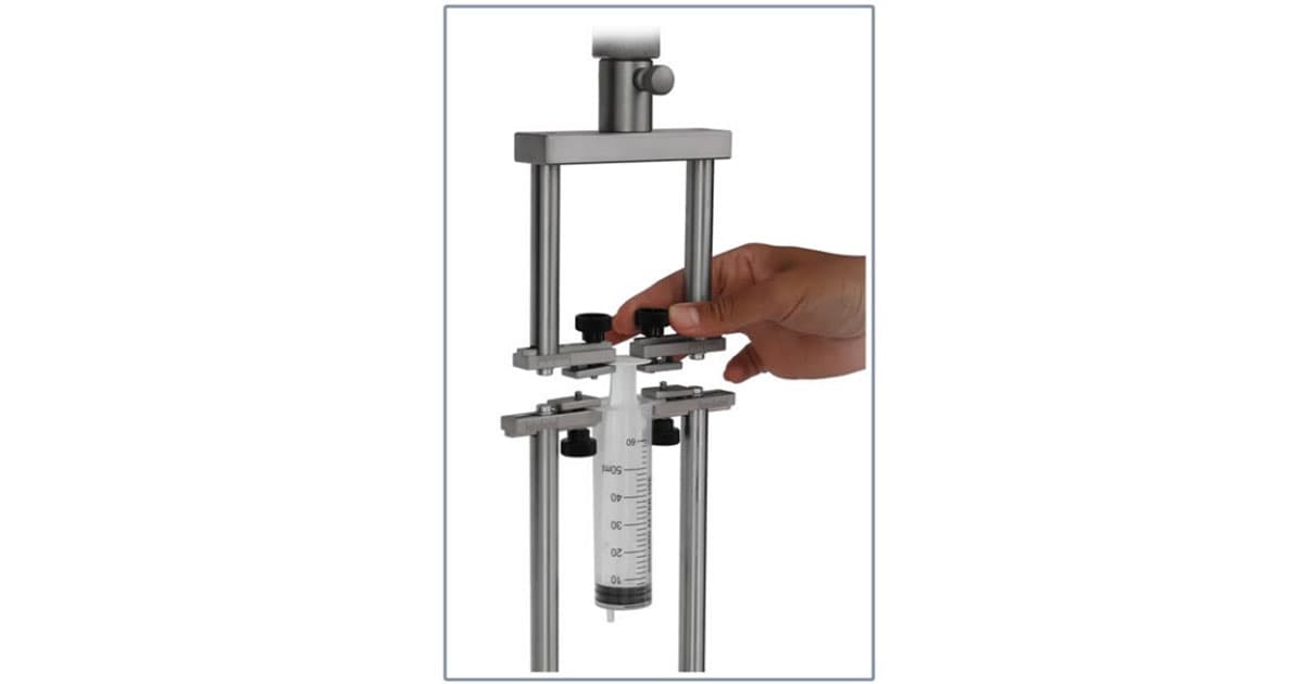 Hand adjusting a syringe held in a metal testing frame for tension or compression testing.