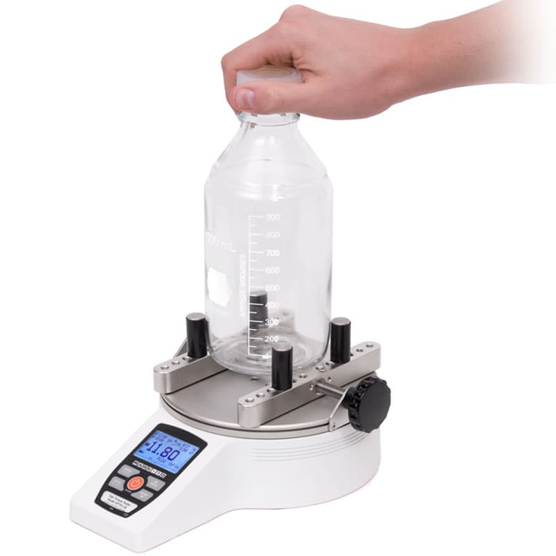 Operator using a Series TT01 Cap Torque Tester to measure cap torque on a large graduated laboratory bottle.