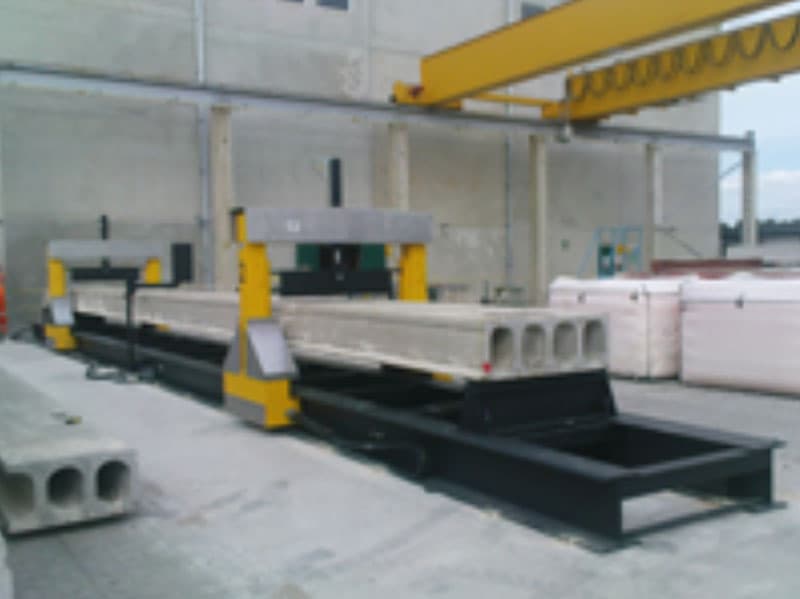 Flexural testing bench with mobile gantries positioned over a precast hollow core concrete slab in an industrial testing facility.